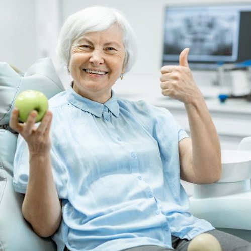 Senior woman with dental implants smiling with thumbs up