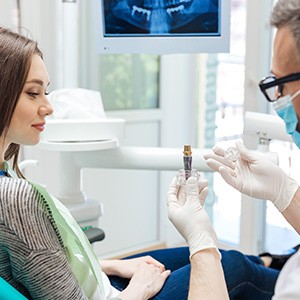 A male dentist showing a dental implant to his female patient