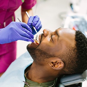 Man in green shirt having dental exam performed by dentist in magenta scrubs