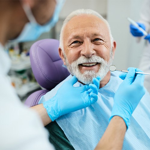 An older smiling man who’s just gotten dentures from his dentist