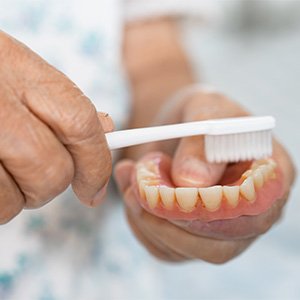 An elderly woman brushing her denture