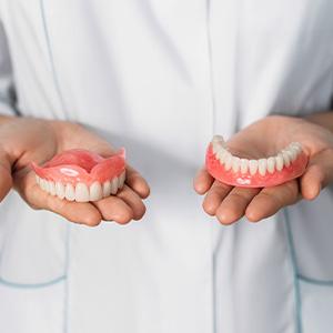 A dentist holding two full dentures in their hands