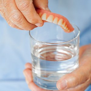 Someone placing dentures in a glass of water