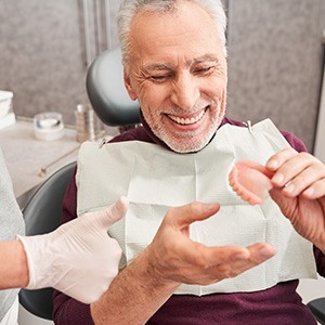 An older man looking at his dentures with a dentist