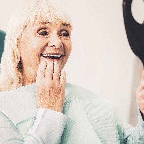 An older woman admiring her new dentures in a hand mirror