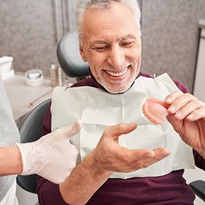 A dentist showing dentures to her older, smiling patient