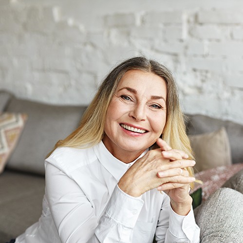 Senior woman sitting on couch smiling with hands folded