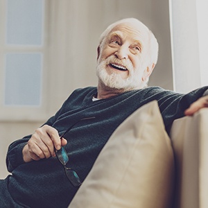 Bearded senior man resting arm on couch and smiling