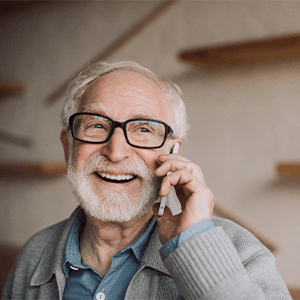 Older man in gray sweater and black glasses smiling talking on cell phone