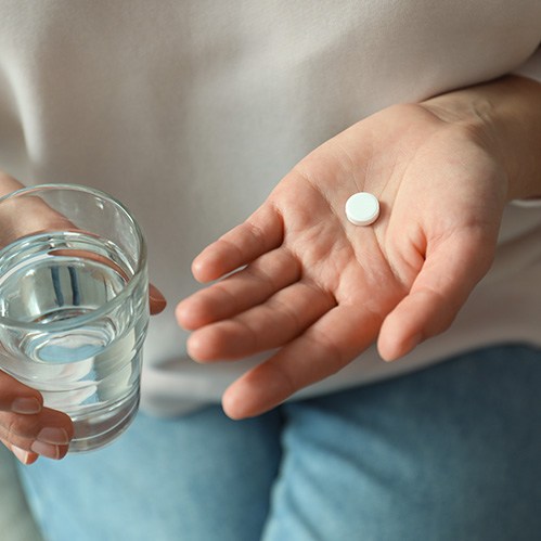 a person holding a glass of water and a pill 