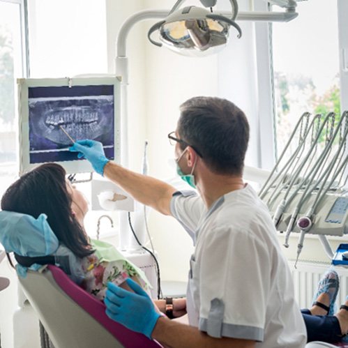 a dentist pointing to an X-ray on a monitor
