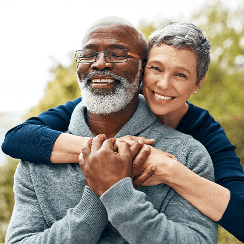 Woman in blue shirt hugging man in gray sweater outside smiling