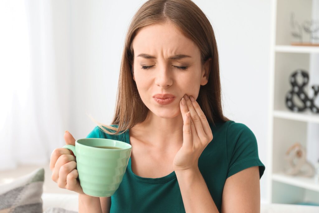 Woman holding green coffee cup pressing fingers to jaw in pain